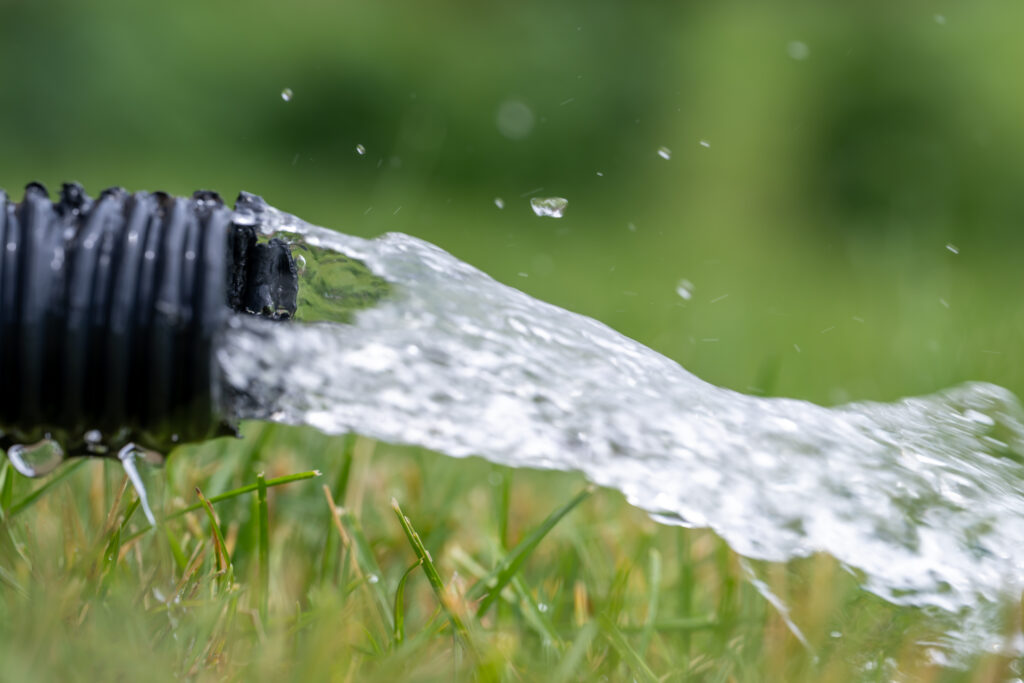 Residential sump pump drain line discharging water into grass yard after a rainstorm